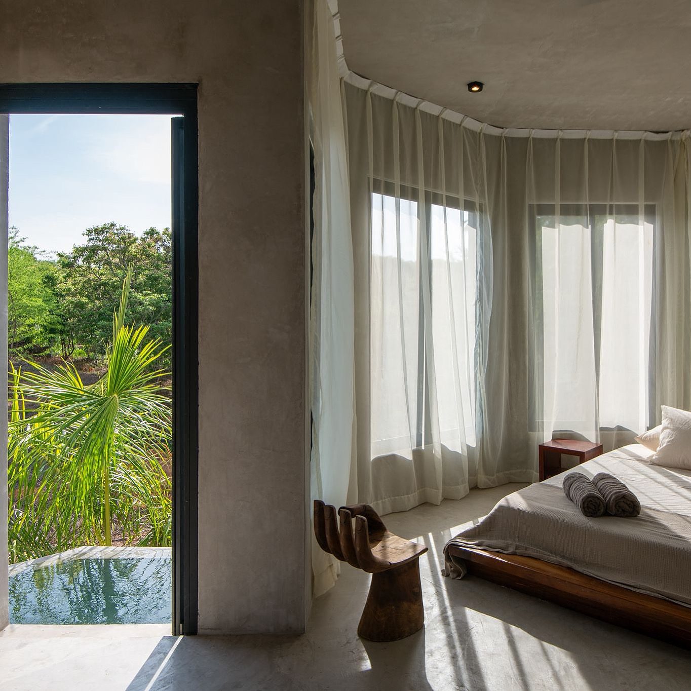 Garden-side bedroom wrapped in soft curtains and tropical greenery, opening onto a private plunge pool