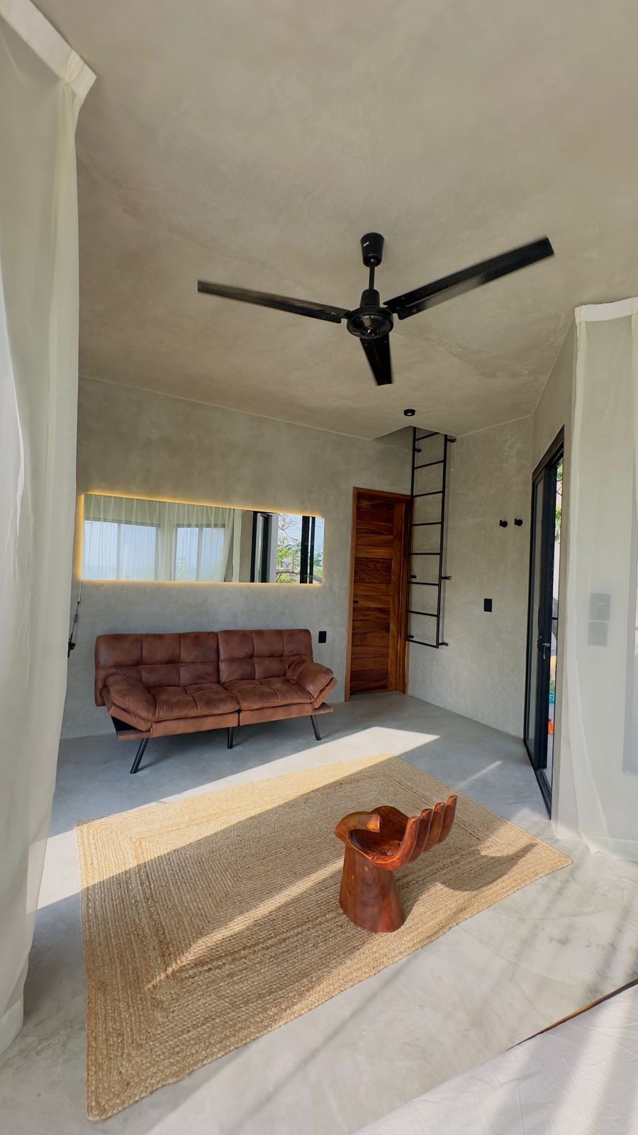 Concrete lounge in the ocean-side suite with a leather sofa, ceiling fan and sculptural wood chair