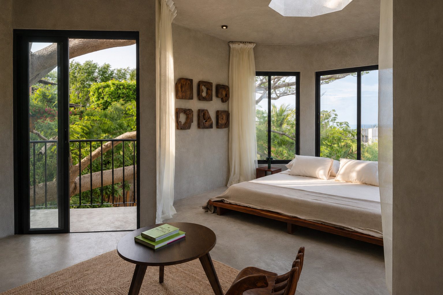Ocean-side bedroom with a king bed, tree branches and a glimpse of the sea through the windows